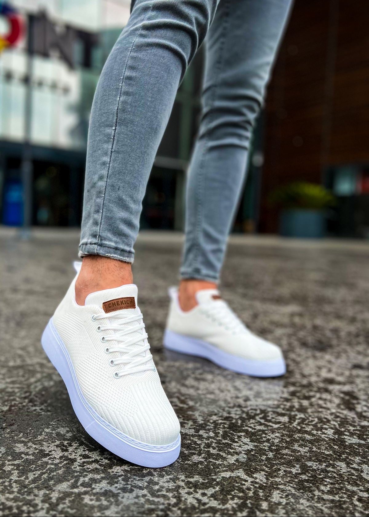 A person wearing white knitted casual shoes with lace-up closure, standing on a concrete surface.