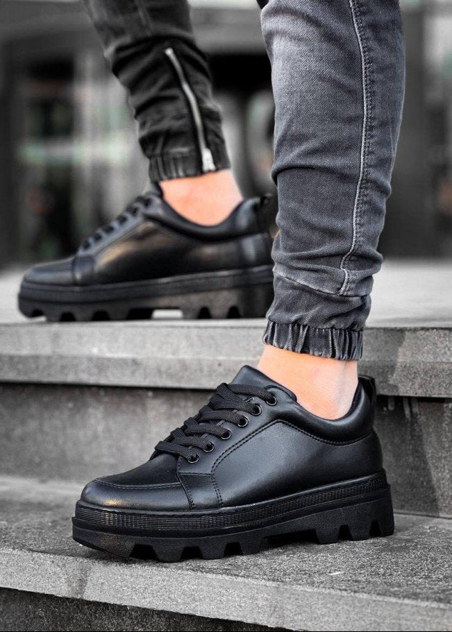Person wearing black leather shoes with thick soles on a concrete surface.