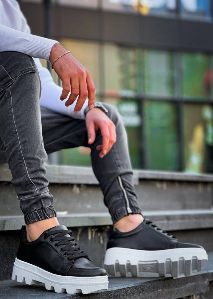 Person wearing black sneakers with white soles on a blurred outdoor background