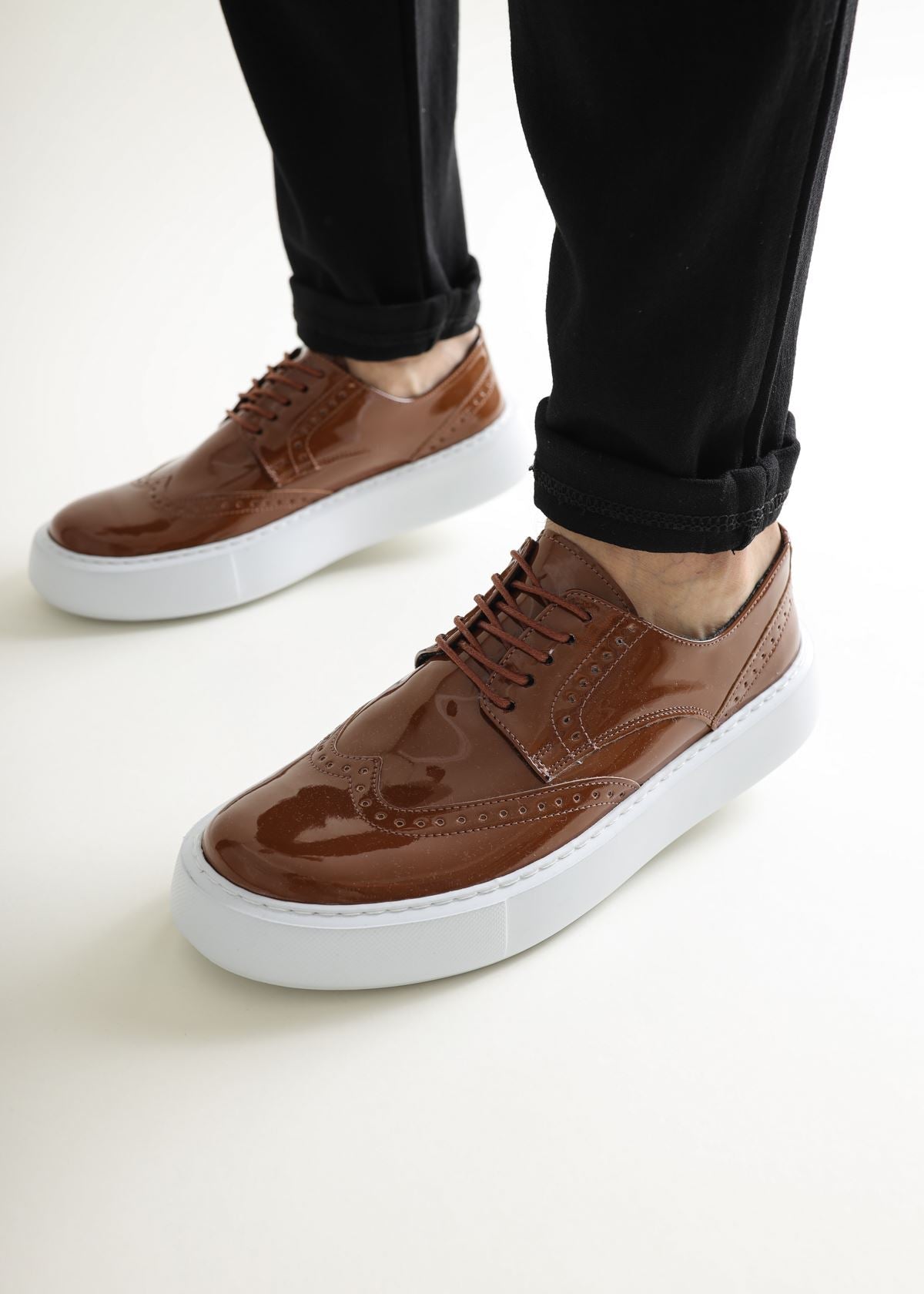 Brown leather shoes with white soles worn with black pants on a light background