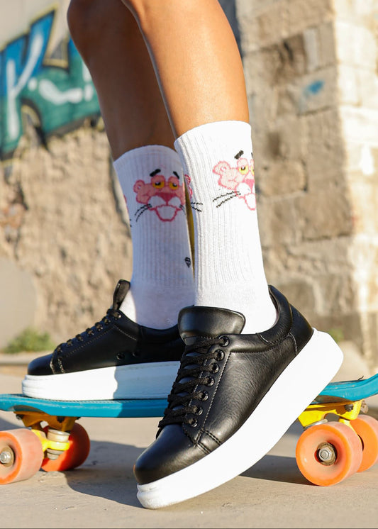 A woman's foot wearing a black sneaker with white sole, placed on a skateboard which is on a colorful surface.