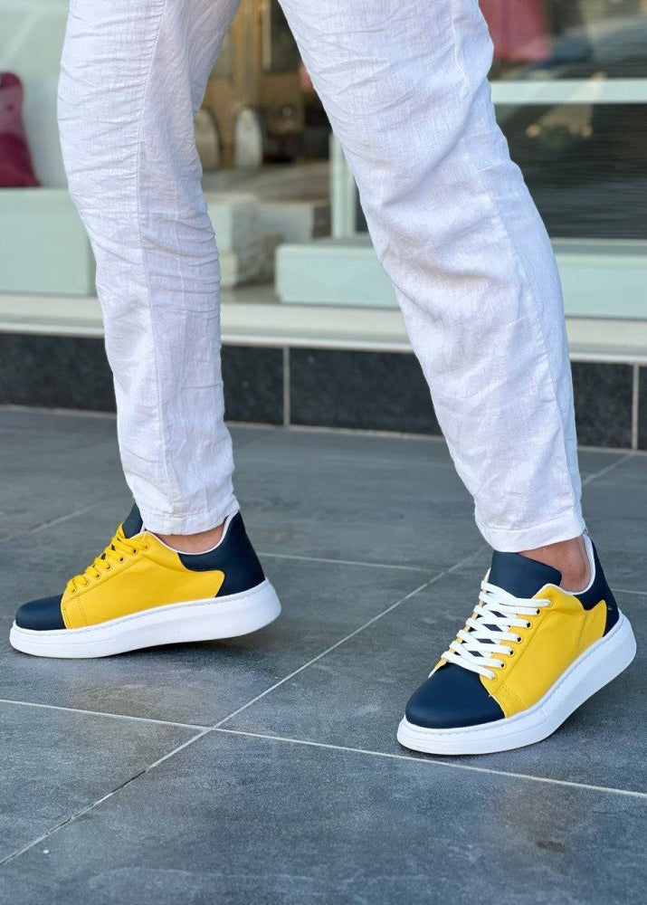 Yellow and navy sneakers worn with white pants on a tiled floor.