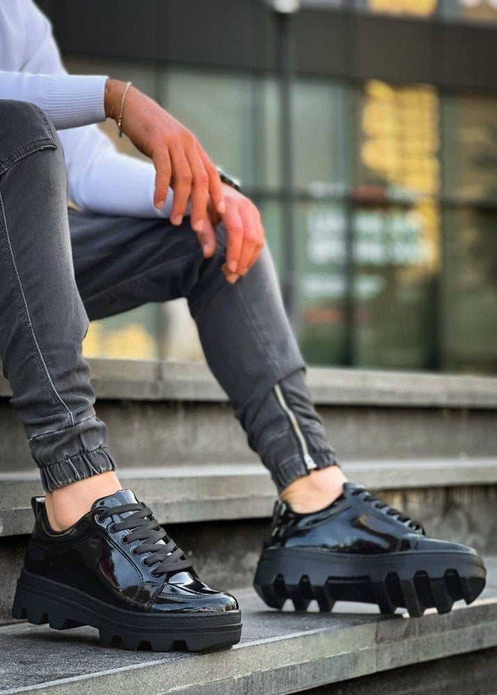 Person wearing black glossy shoes on a concrete surface with blurred background
