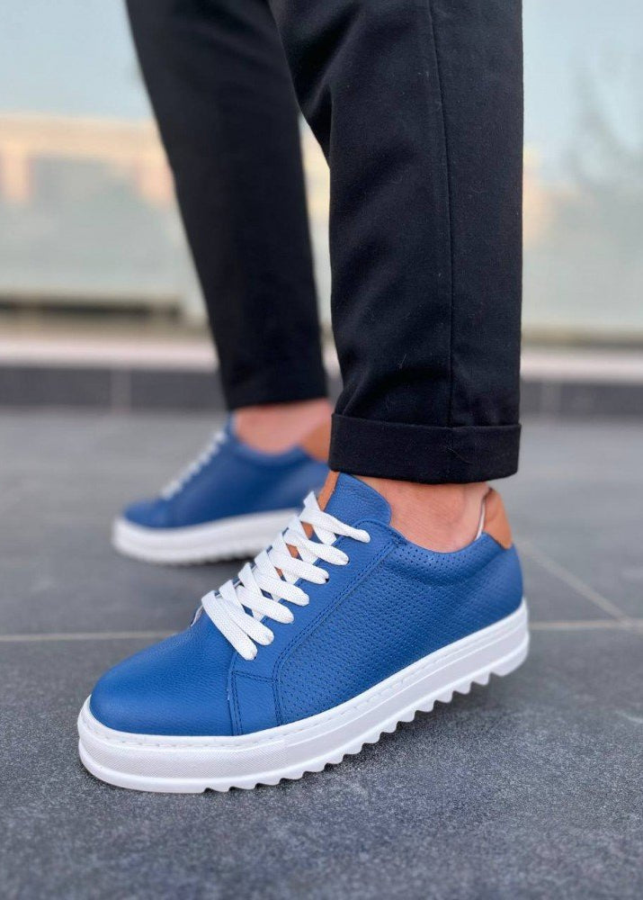 Blue sneakers with white soles worn by a person on a gray pavement.