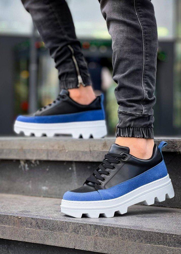 Black and blue sneakers with white soles worn by a person on steps.
