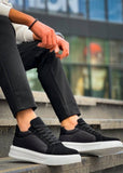 Black sneakers with white soles worn by a person sitting on steps.
