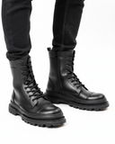 Lifestyle shot of Orion Black Combat Boots by Apollo Moda in polished leather with rugged soles and zip detail 