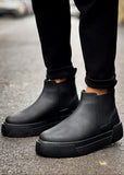 Close-up of matte black Avalon Chelsea boots worn outdoors with cuffed pants.