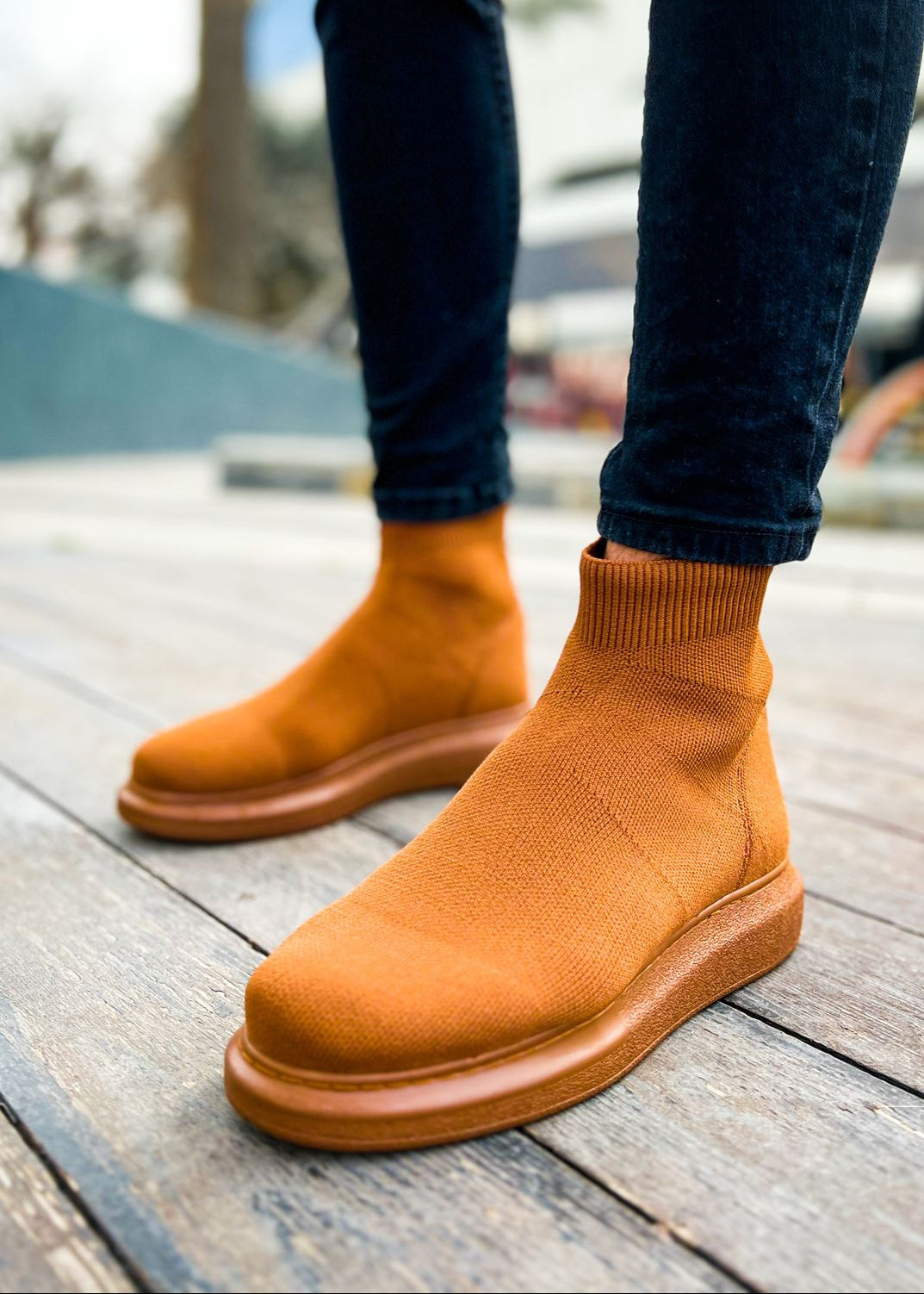 A pair of men's light brown knit ankle boots on a wooden surface, showcasing the boots' height-enhancing soles and the style of the footwear.