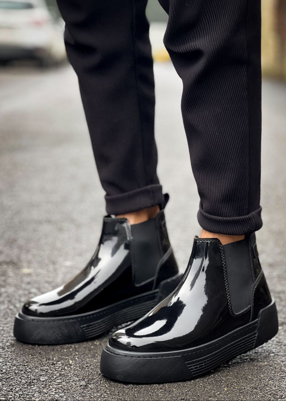 Close-up of black patent Avalon Chelsea Apollo boots worn outdoors with black pants.