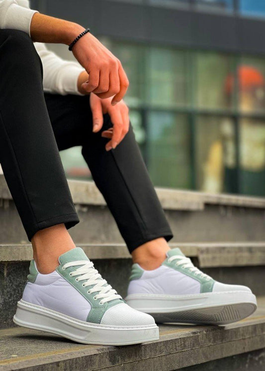 White and green sneakers worn by a person sitting on steps.