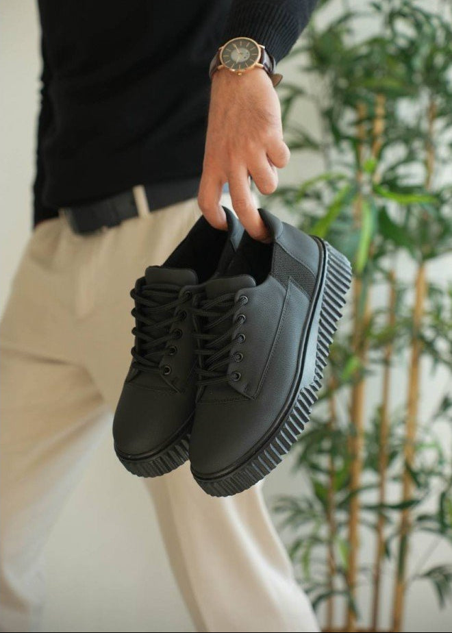 Person holding a pair of black sneakers with a blurred background